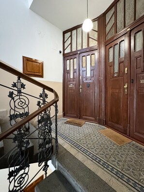 A staircase with ornate metal railings, a wooden door with glass panels, and patterned floor tiles.