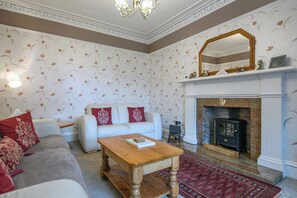 A living room with a white sofa, a wooden coffee table, a patterned rug, a fireplace, and a decorative mirror.
