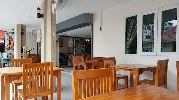 A restaurant with wooden tables and chairs, a fan, and a view of the street through windows. - Welcome Inn Hotel Karon Beach (Karon)