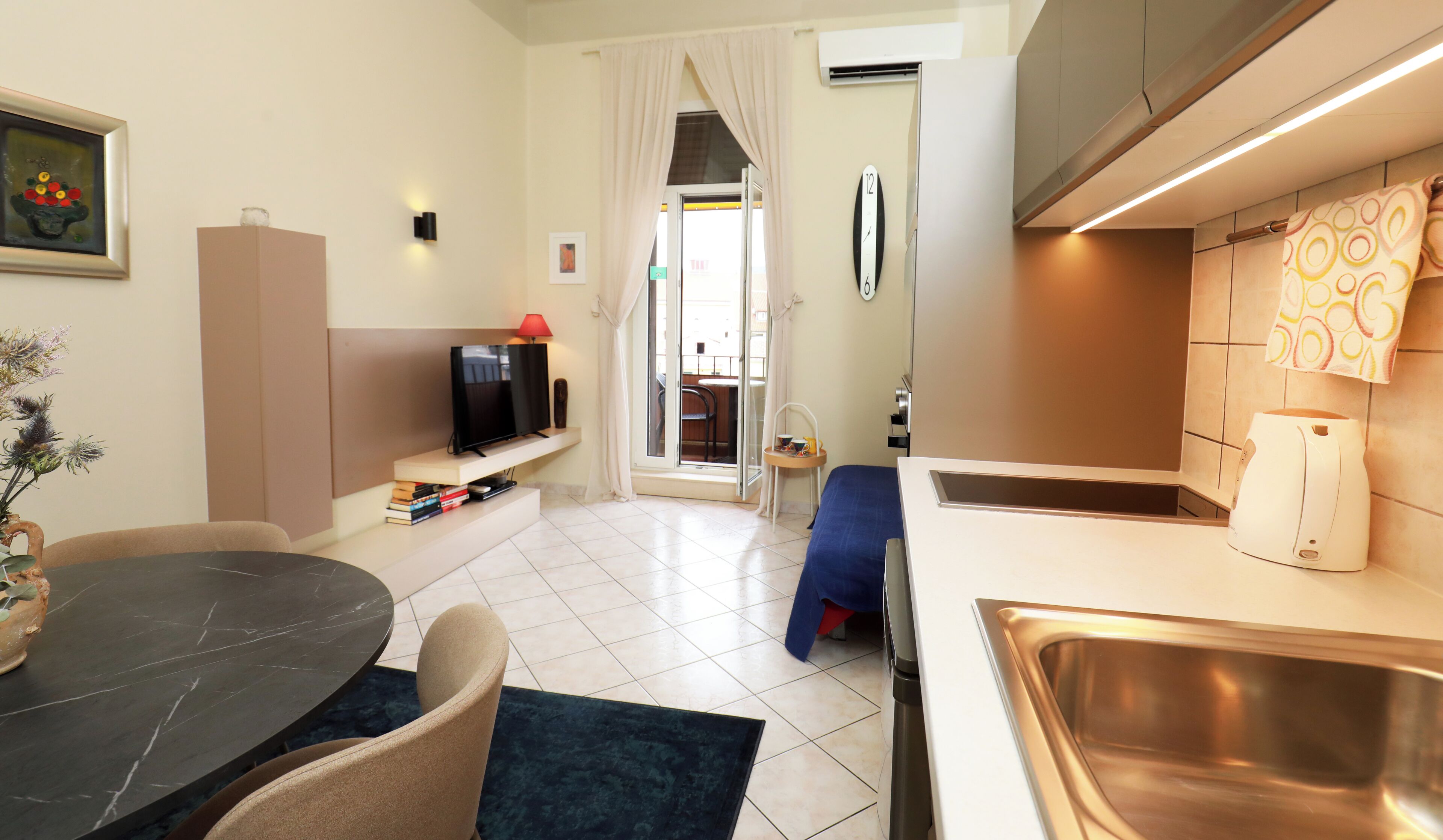Habitación de hotel compacta con comedor, kitchenette y vistas a través de una puerta.