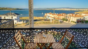 Un balcón con vista a un pueblo costero, una mesa de madera y dos sillas de madera.