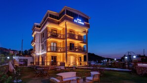 Un hotel de varios pisos con un balcón en el segundo piso, zona de estar al aire libre y un cartel con el nombre 'Cimco Bal Konak'.