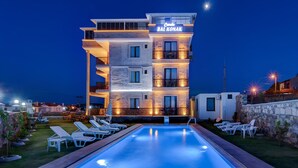 Un hotel moderno con piscina, sillones de descanso y fachada bien iluminada.