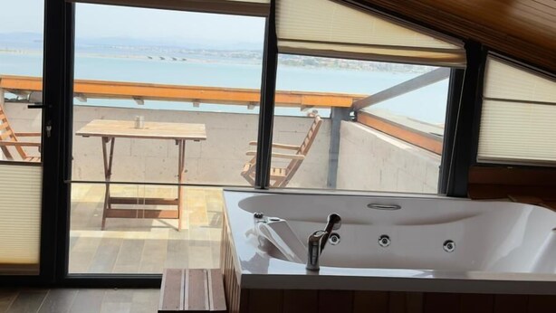 Un dormitorio moderno con un ventanal grande, techo de madera, bañera y vistas al mar.