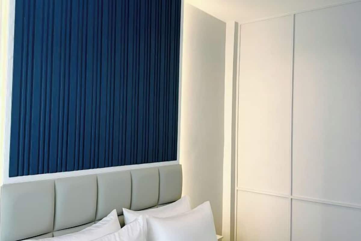 A bedroom with a bed, a window with a blue curtain, and a white wardrobe.
