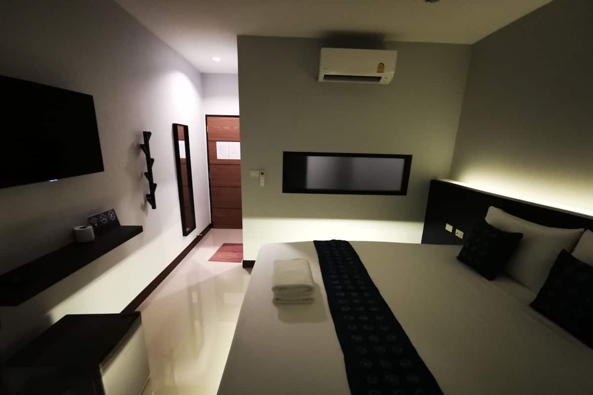 A modern hotel room with a large bed, a flat-screen TV mounted on the wall, a built-in air conditioning unit, and a small shelf with a remote control.
