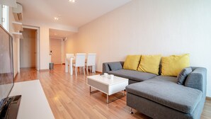 Un salon moderne avec un canapé gris, deux coussins jaunes, une table basse blanche et un coin repas comprenant des chaises et une table blanches.