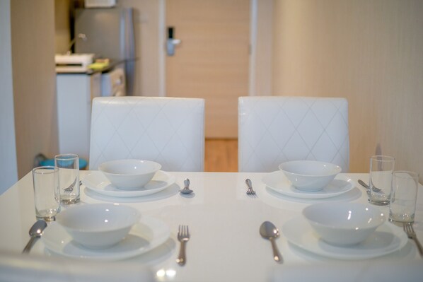 A dining table set with white plates, bowls, and cutlery, with two chairs at each end.