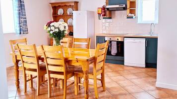 A compact kitchen with a dining table, chairs, a refrigerator, a dishwasher, and a wooden cabinet with dishes.
