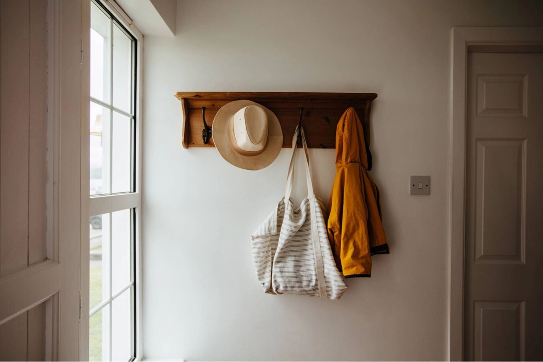 Een kamer met een houten kapstok, een hoed, een gestreepte tas en een geel jasje aan de muur.