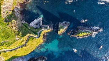An aerial view of a coastal area with a winding road, rocky outcrops, and clear blue waters.