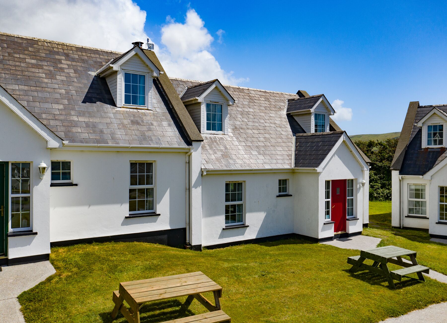 A row of white cottages with grey roofs, a red door, and a picnic table in the foreground.