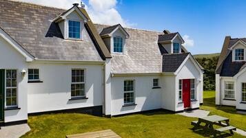 A row of white cottages with grey roofs, a red door, and a picnic table in the foreground.