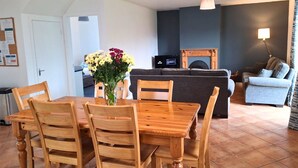 Un coin repas avec une table et des chaises en bois, un vase de fleurs, un canapé, un téléviseur et une lampe.