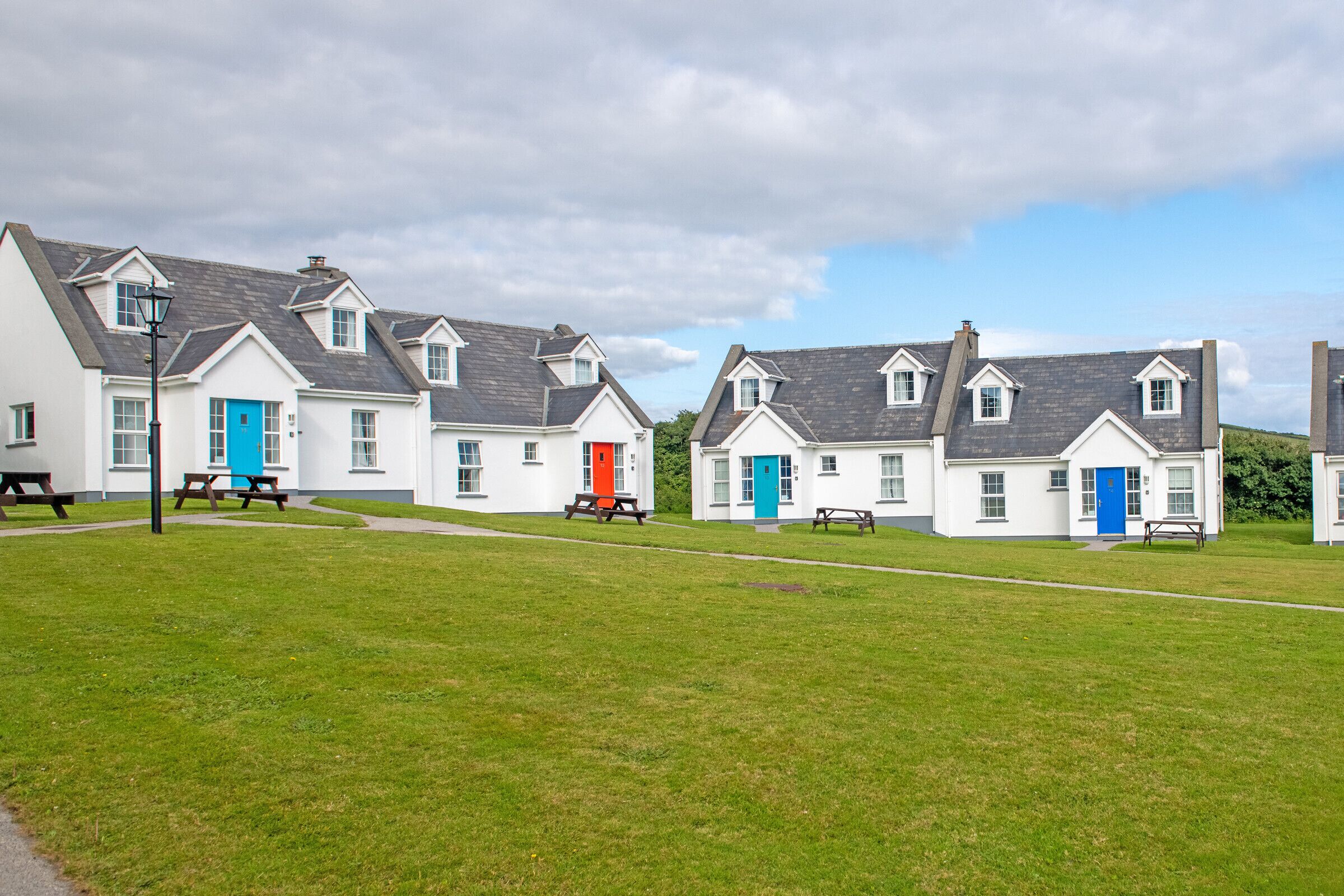 A row of white cottages with blue and red doors, each with a picnic table in front.