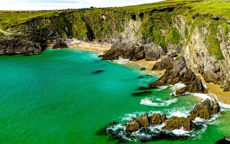 Un paisaje costero con una playa, acantilados rocosos y agua turquesa cristalina.