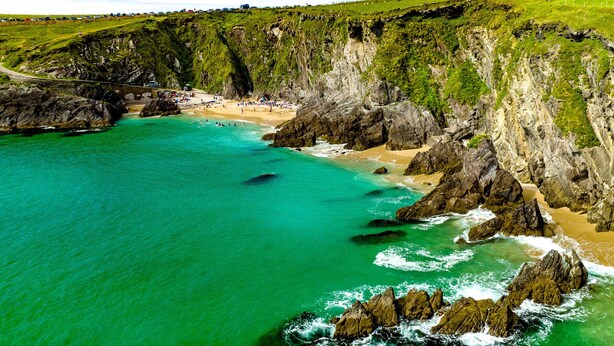 Un paysage côtier avec une plage, des falaises rocheuses et une eau turquoise cristalline.