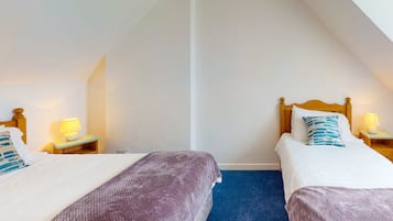 Ein Zimmer mit zwei Betten, jeweils mit einem hölzernen Kopfteil, einem blauen Teppich und Nachttischlampen.