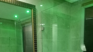 Un baño con lavamanos blanco, tocador morado, un espejo con marco decorativo, ducha con cerramiento de vidrio y bañera con tonalidad verdosa.