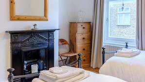Un dormitorio con chimenea, un aparador de madera, una ventana con cortinas y una cama con toallas.