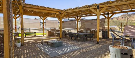 An outdoor patio area with wooden pergolas, tables, chairs, and a barbecue grill.