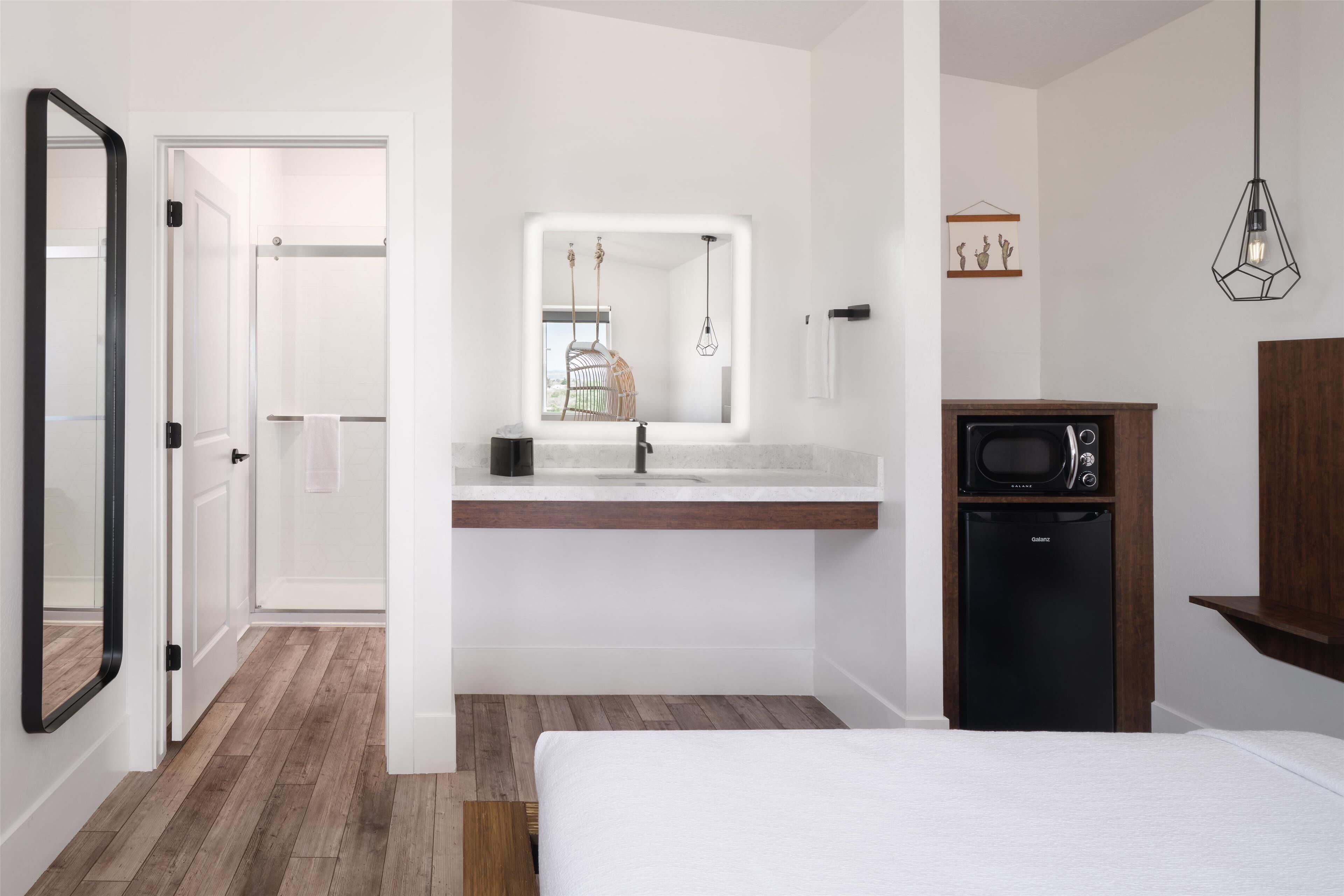 Ein modernes Hotelzimmer mit Holzboden, einem Bett, einem eingebauten Waschbecken mit Spiegel, einer Mikrowelle und einer hängenden Leuchte.