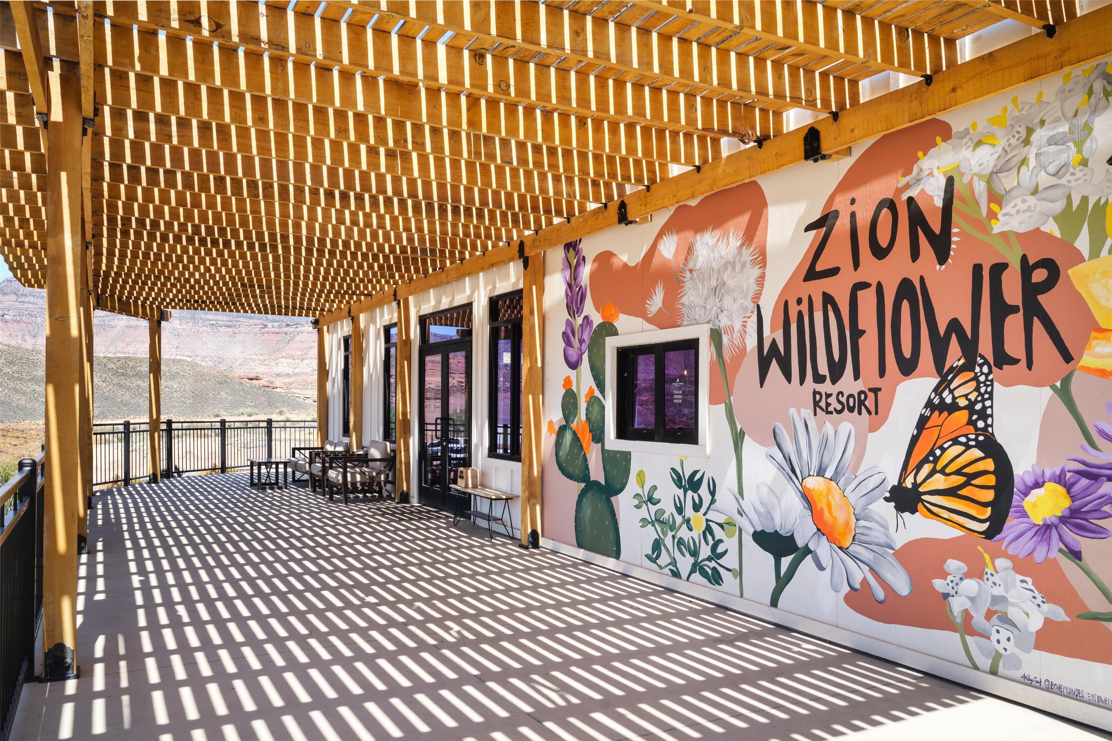 A covered outdoor area with a wooden ceiling, a mural with flowers and text, and a view of a desert landscape.