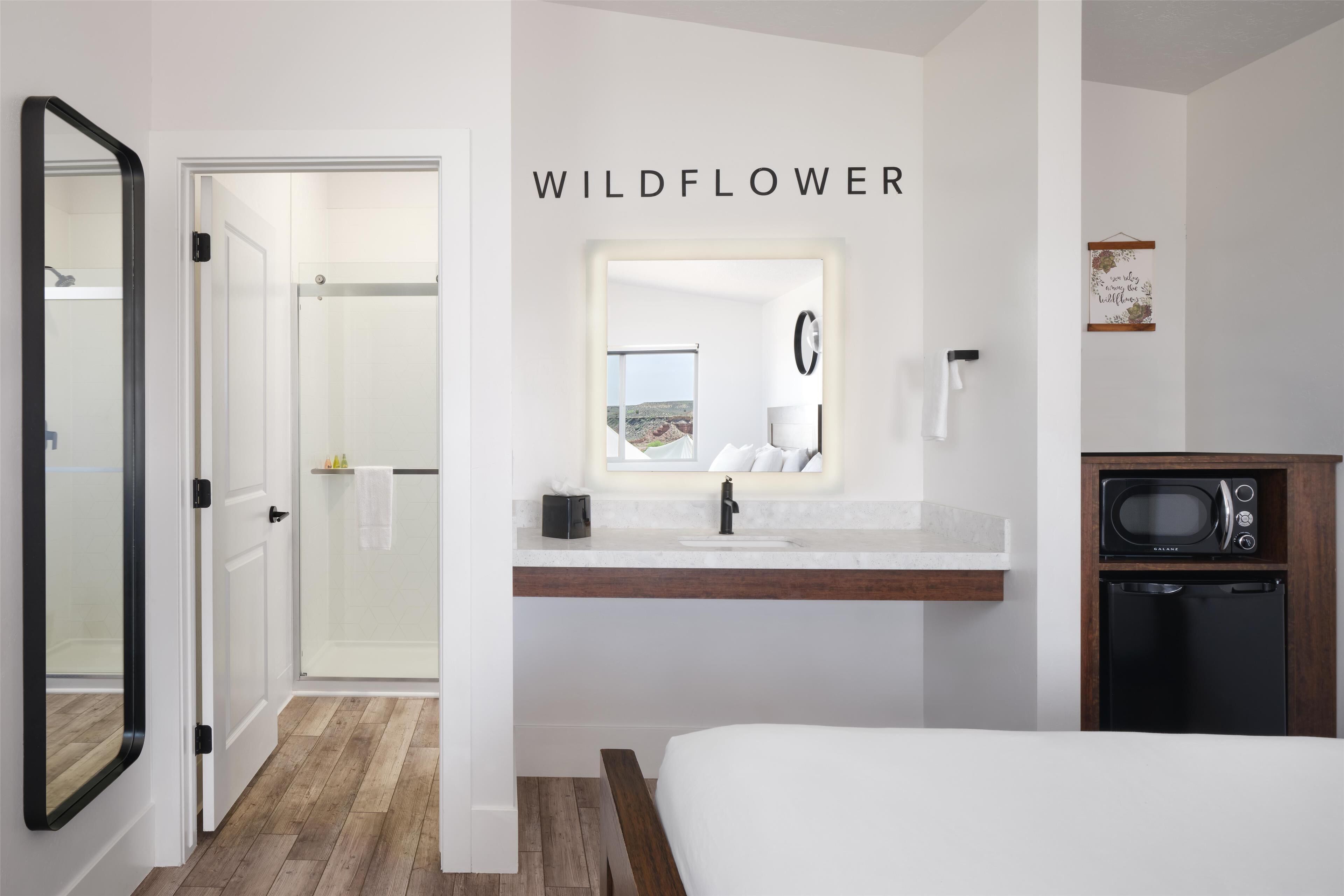 Ein Schlafzimmer mit Bett, ein Badezimmer mit Waschbecken und Spiegel sowie eine Mikrowelle.