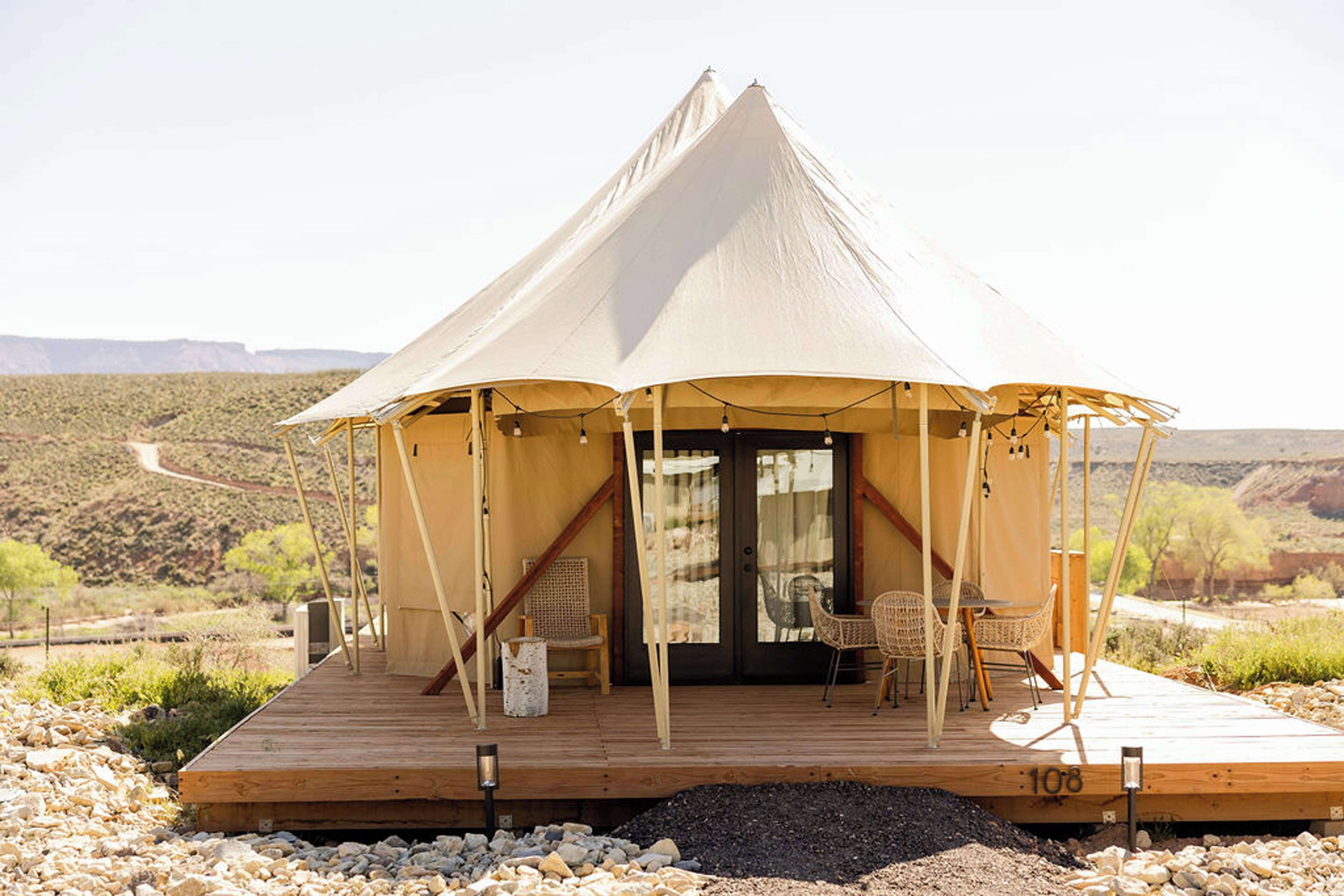 A tented accommodation with a wooden deck, outdoor seating, and a view of the desert landscape.