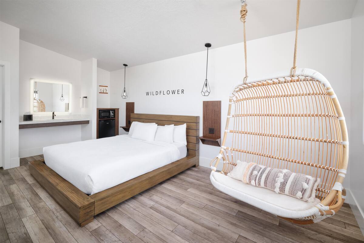 Quarto com cama de madeira, cadeira suspensa, espelho e prateleira na parede.