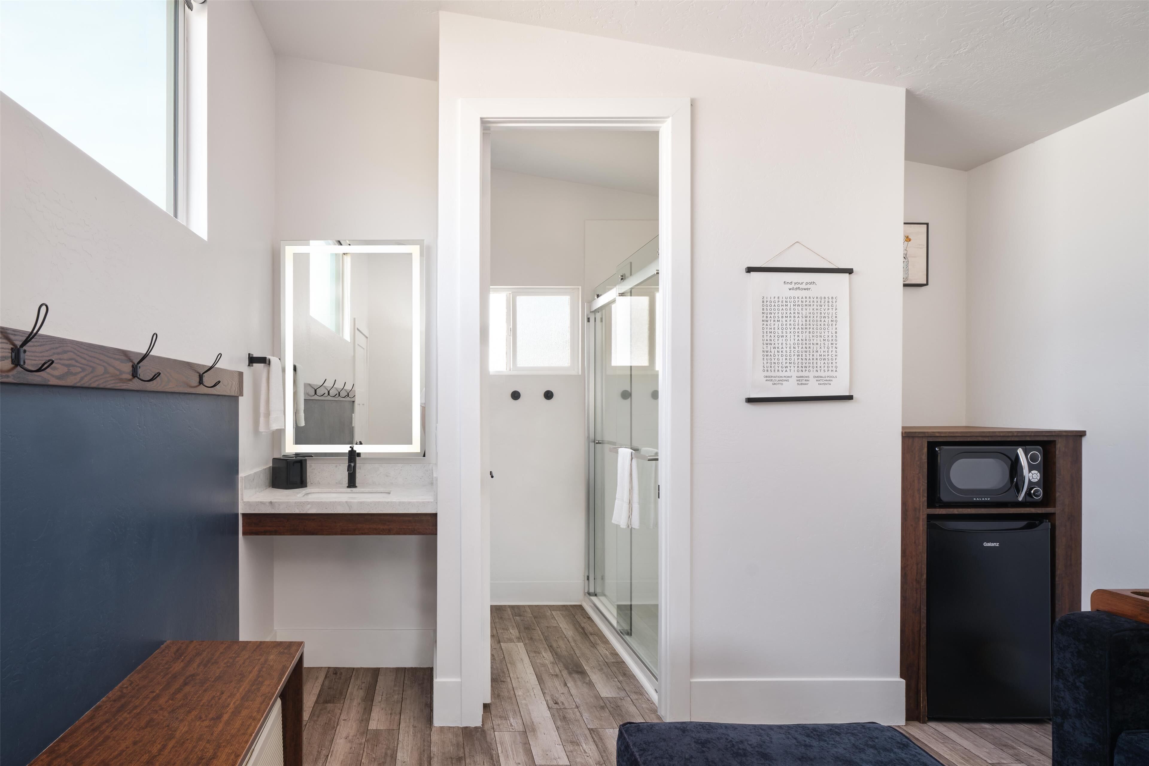 Een moderne badkamer met een houten bankje, een wastafel met spiegel, een douche en een magnetron.