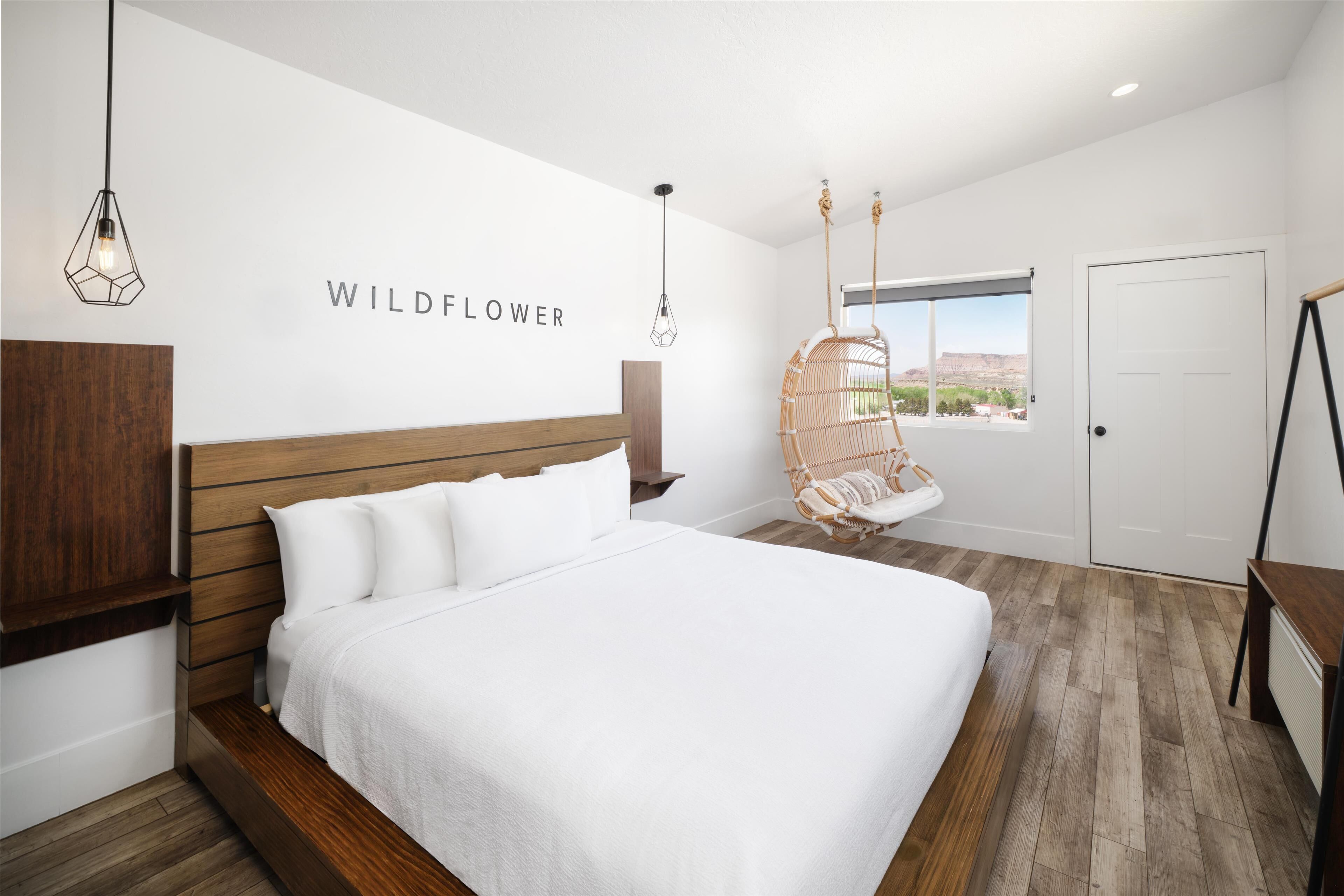 A bedroom with a large bed, a hanging chair, a wooden headboard, and a window with a view.