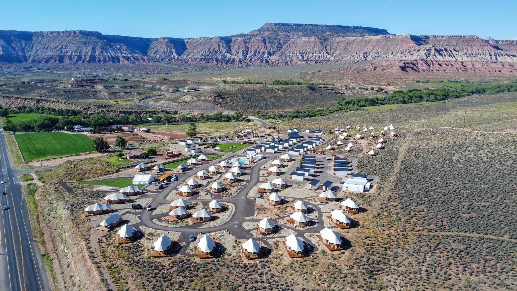 An aerial view of a resort with multiple dome-shaped tents arranged in rows, surrounded by a desert landscape with mountains in the background.