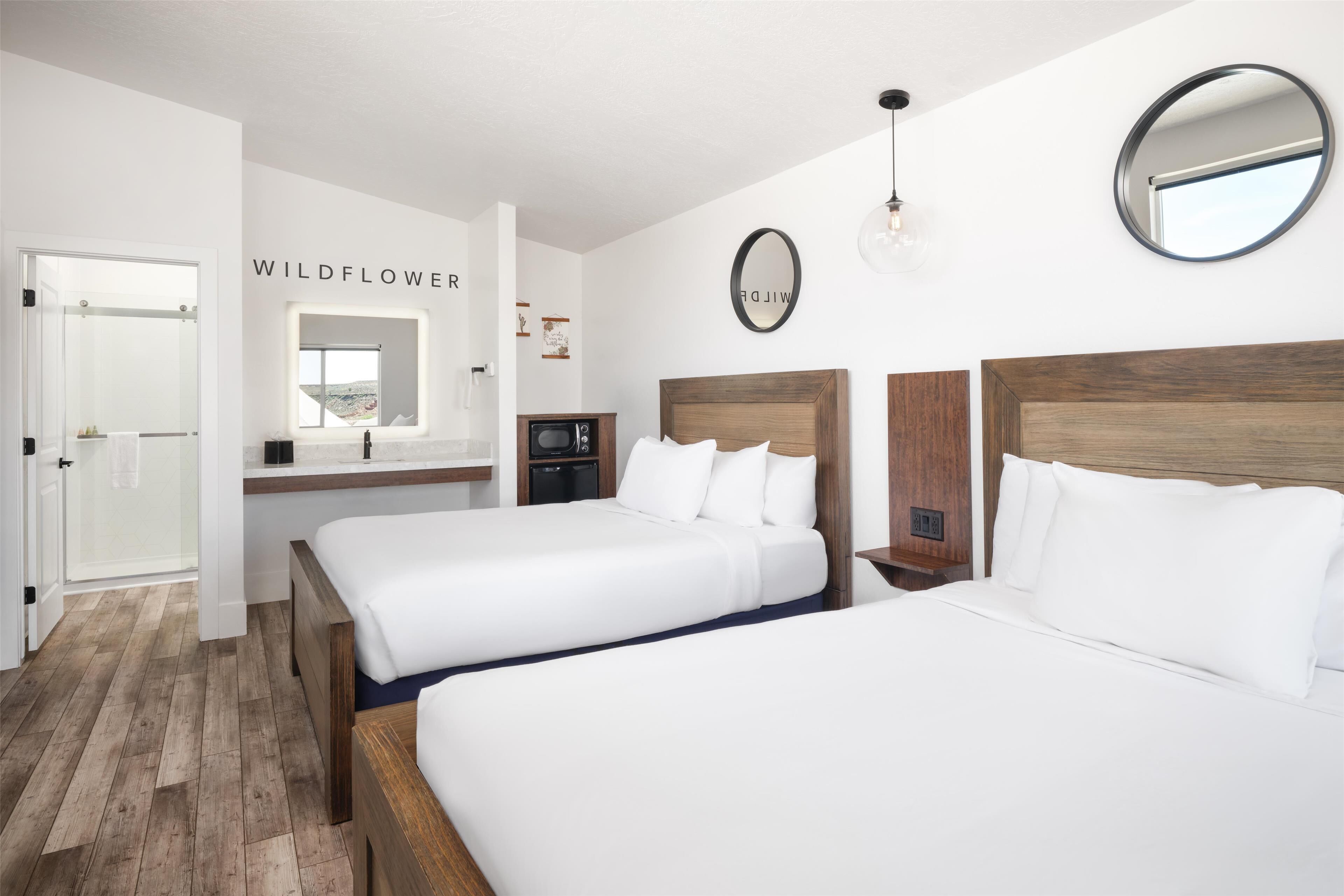 A hotel room with two beds, a wooden floor, a small kitchenette, and a mirror on the wall.