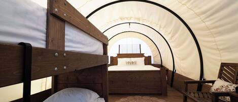 Una habitación con carpa, dos literas de madera, una silla de madera y una alfombra tejida.