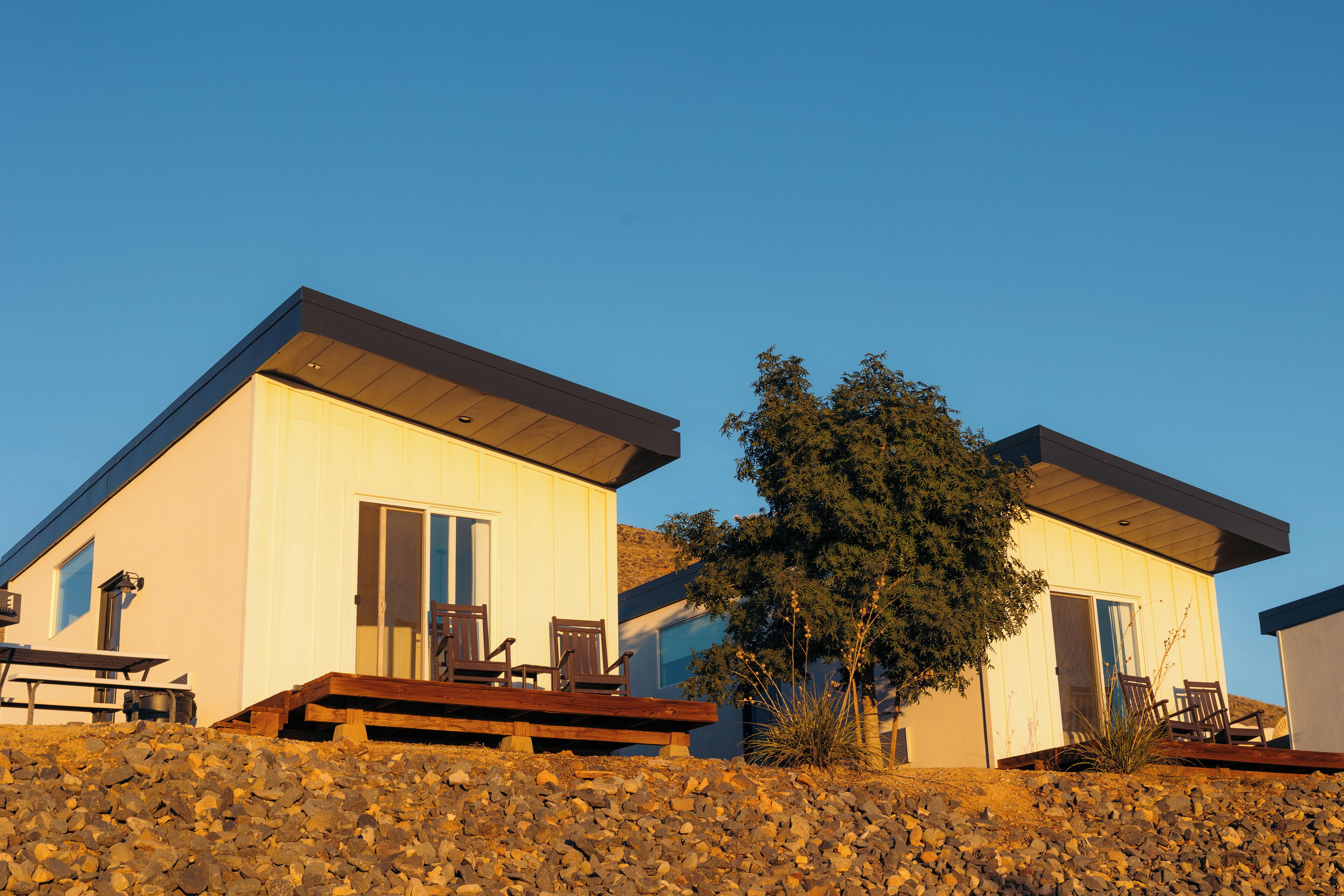 Two modern houses with a patio and a stone wall in front.