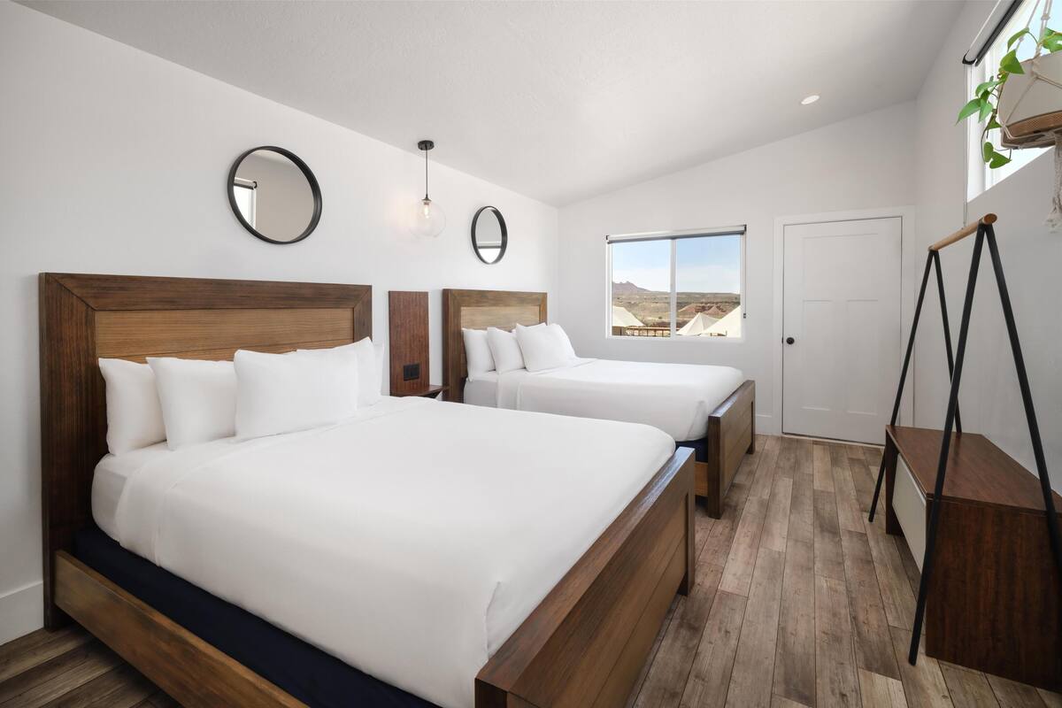 Quarto com duas camas, uma janela ampla com vista e uma planta no parapeito.