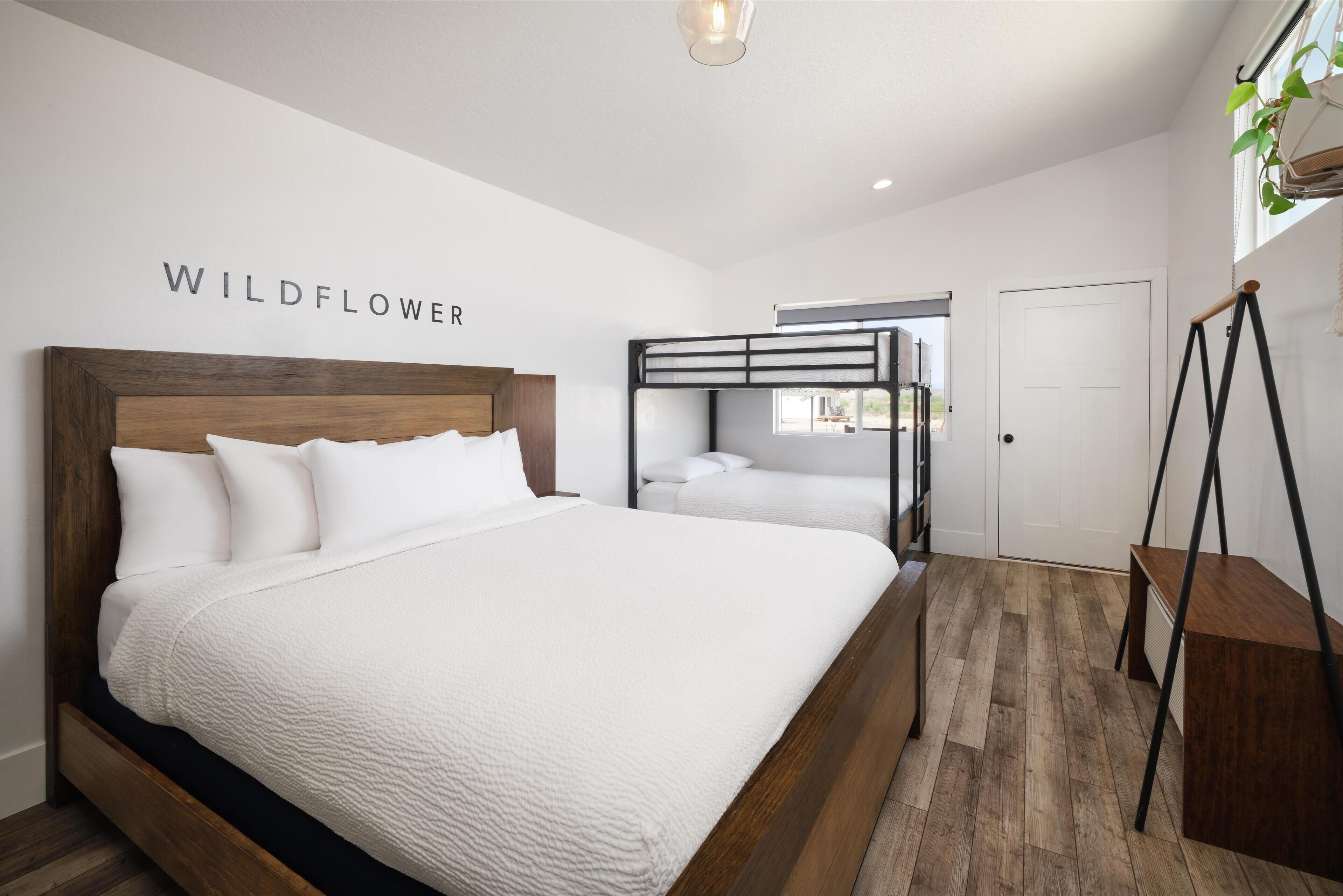 Une chambre avec un grand lit, un lit superposé, un plancher en bois et une plante fixée au mur.