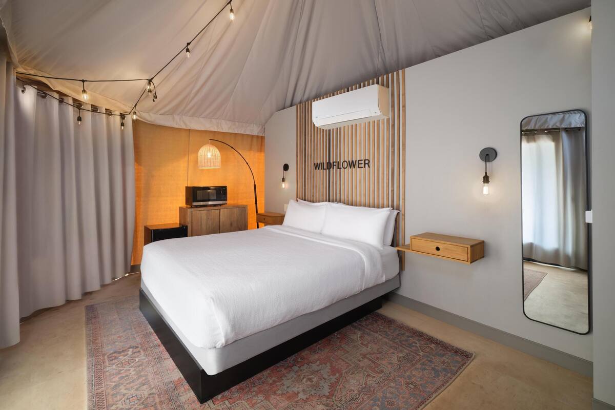 Quarto com uma cama grande, mesa de cabeceira, espelho e ar-condicionado fixado na parede.