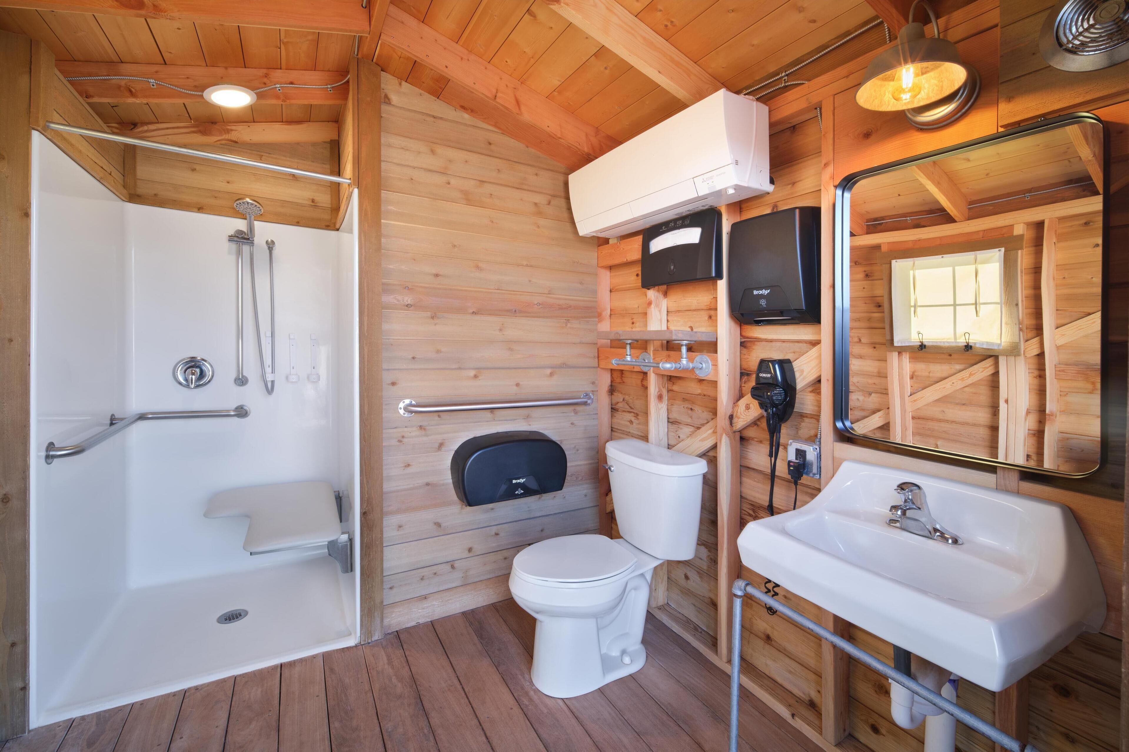Bagno di una baita in legno con doccia, toilette, lavandino e televisione a parete.