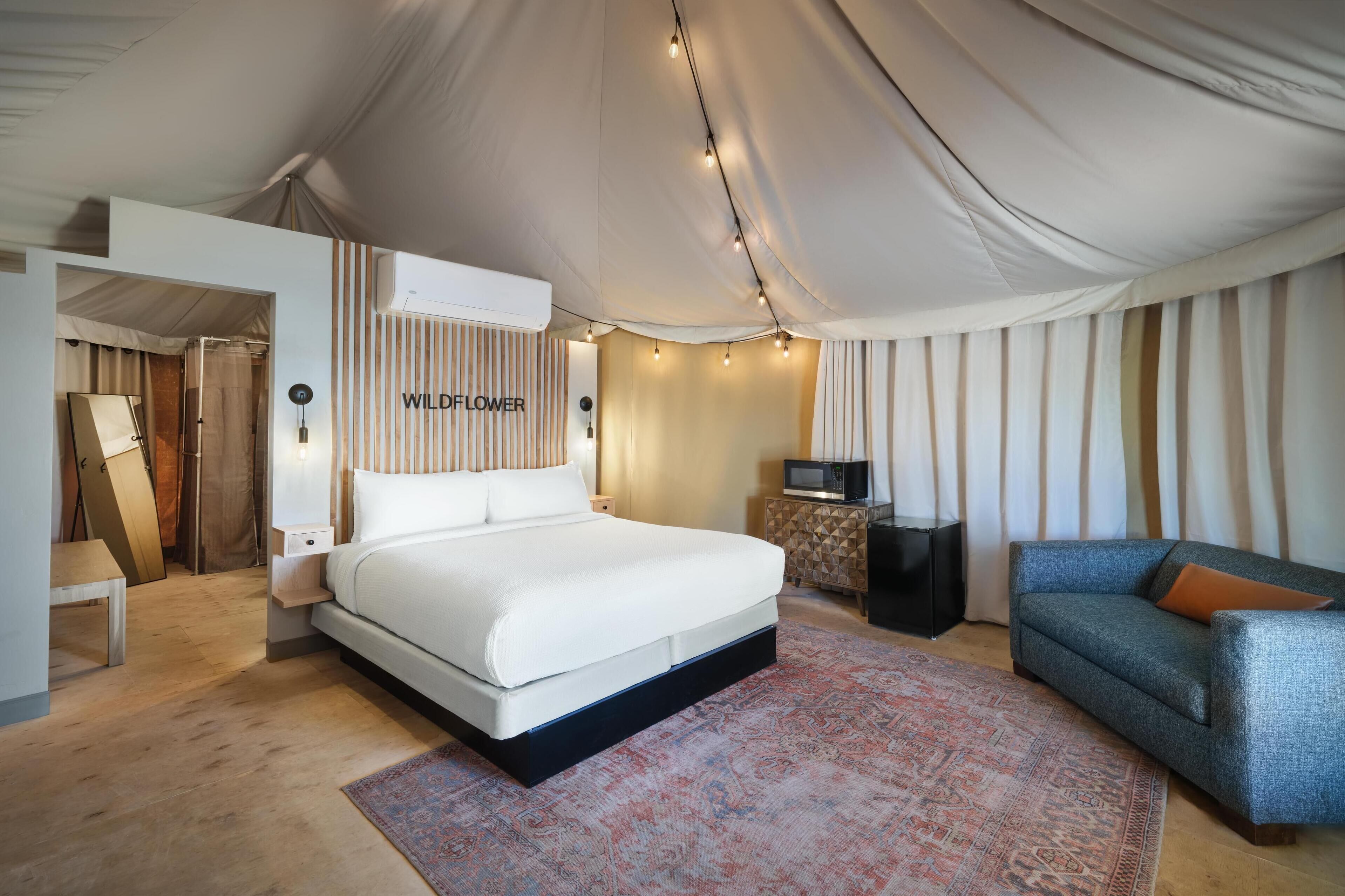 A bedroom with a large bed, a sofa, a TV, and a wall-mounted air conditioner.