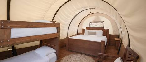 A tent with two wooden bunk beds, a small wooden chair, and a woven rug.