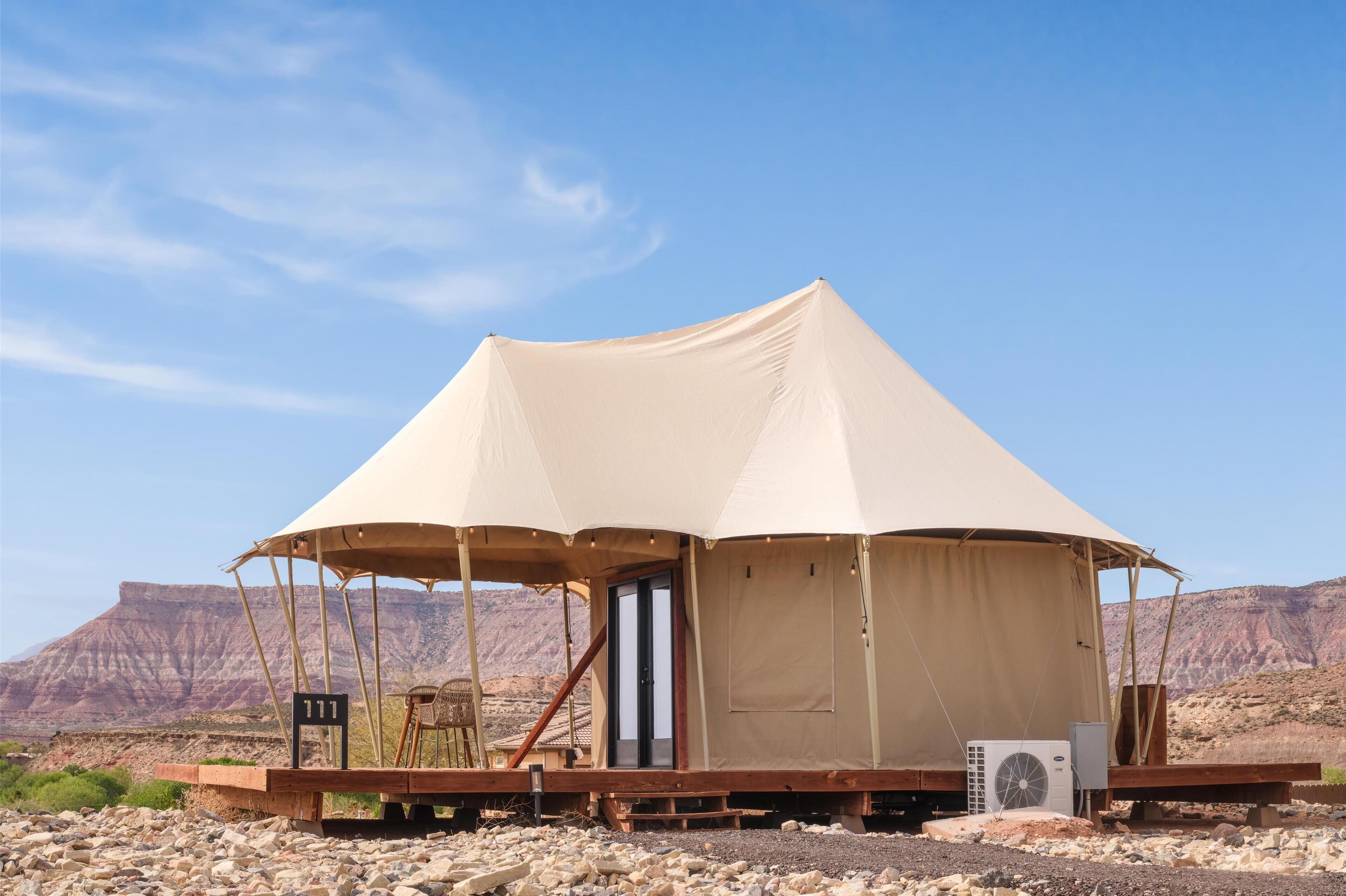 A large, beige tent with a door and windows, set on a wooden platform with steps leading up to it.