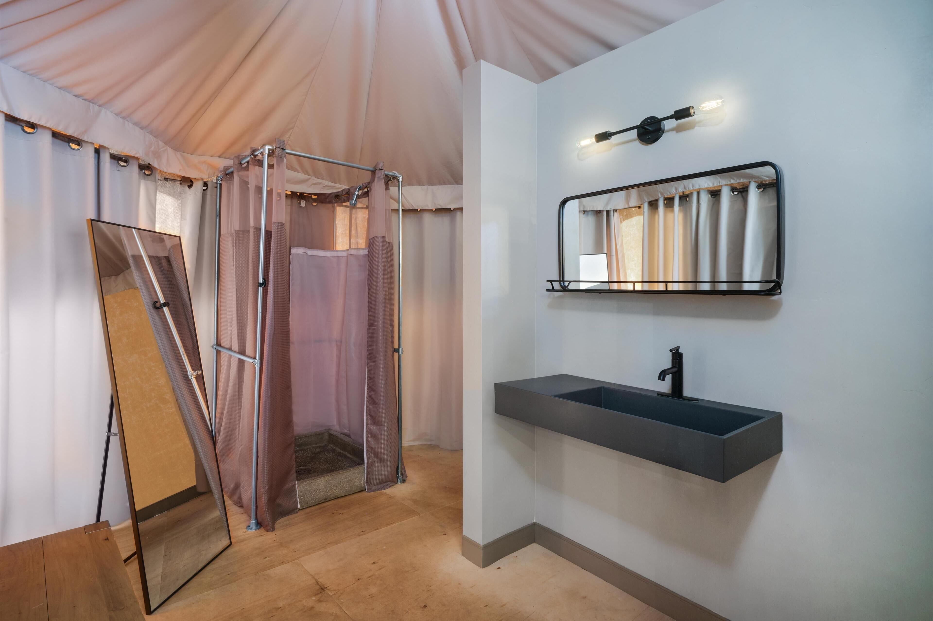 A tented room with a shower enclosure, a mirror, and a sink.