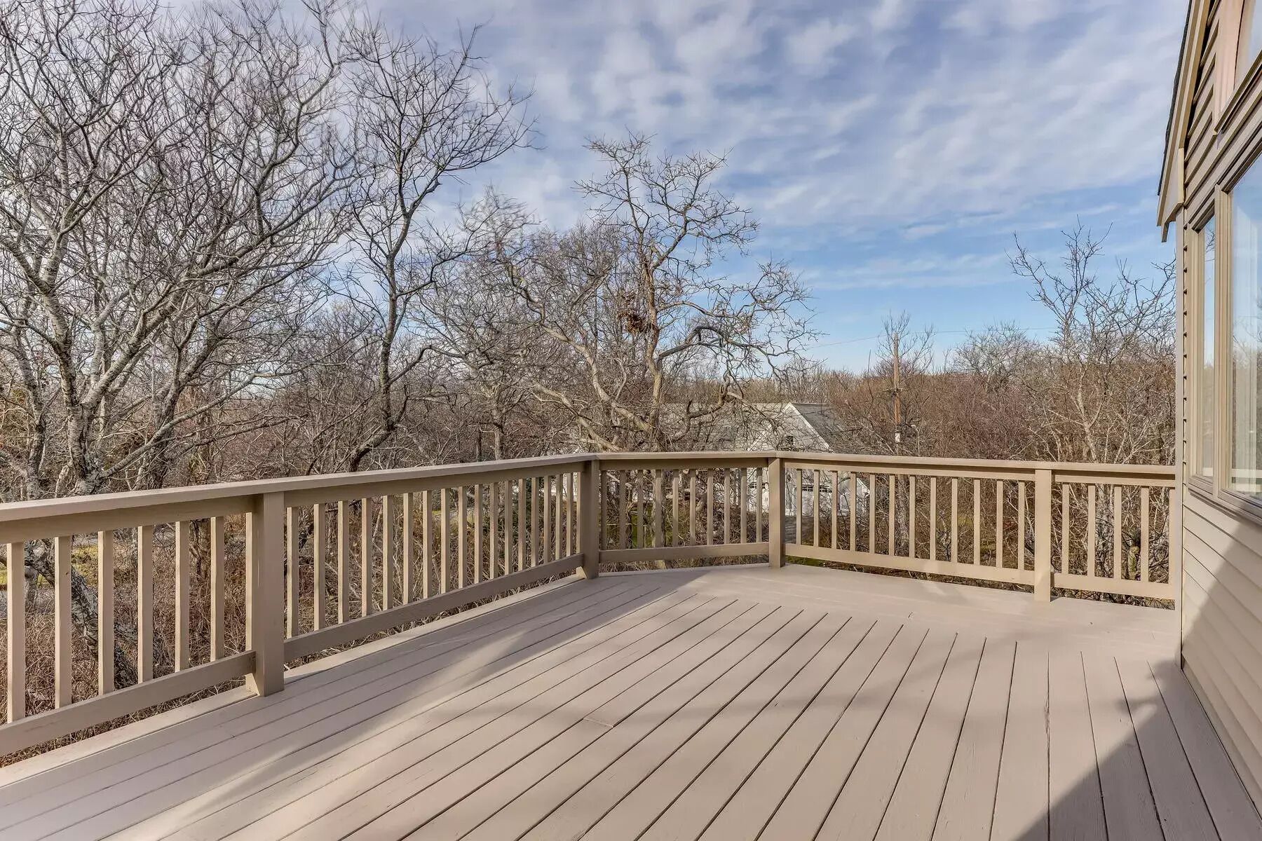 A wooden deck with a railing, surrounded by trees and a clear sky.