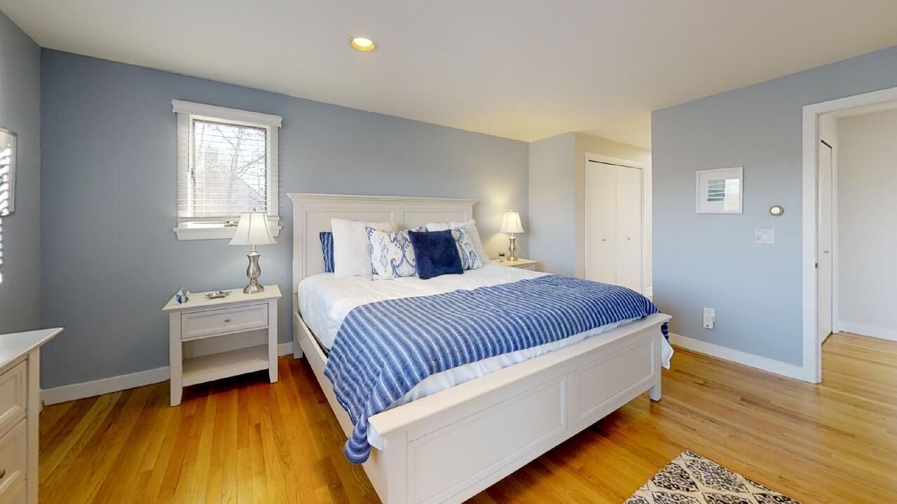 A bedroom with a bed, nightstands, a window, and a door.