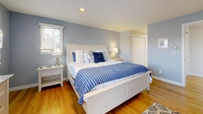 Un dormitorio con cama, mesitas de noche, una ventana y una puerta.