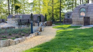 A pathway leading to stone structures with arched windows, surrounded by greenery and trees. - Iglu Camp Heidewald (Sassenberg)