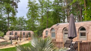 A row of RVs with a covered outdoor seating area and a large plant in the foreground. - Iglu Camp Heidewald (Sassenberg)