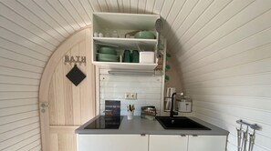 A compact kitchen with a built-in sink, a small countertop, and a shelf above the sink holding dishes and utensils. - Iglu Camp Heidewald (Sassenberg)